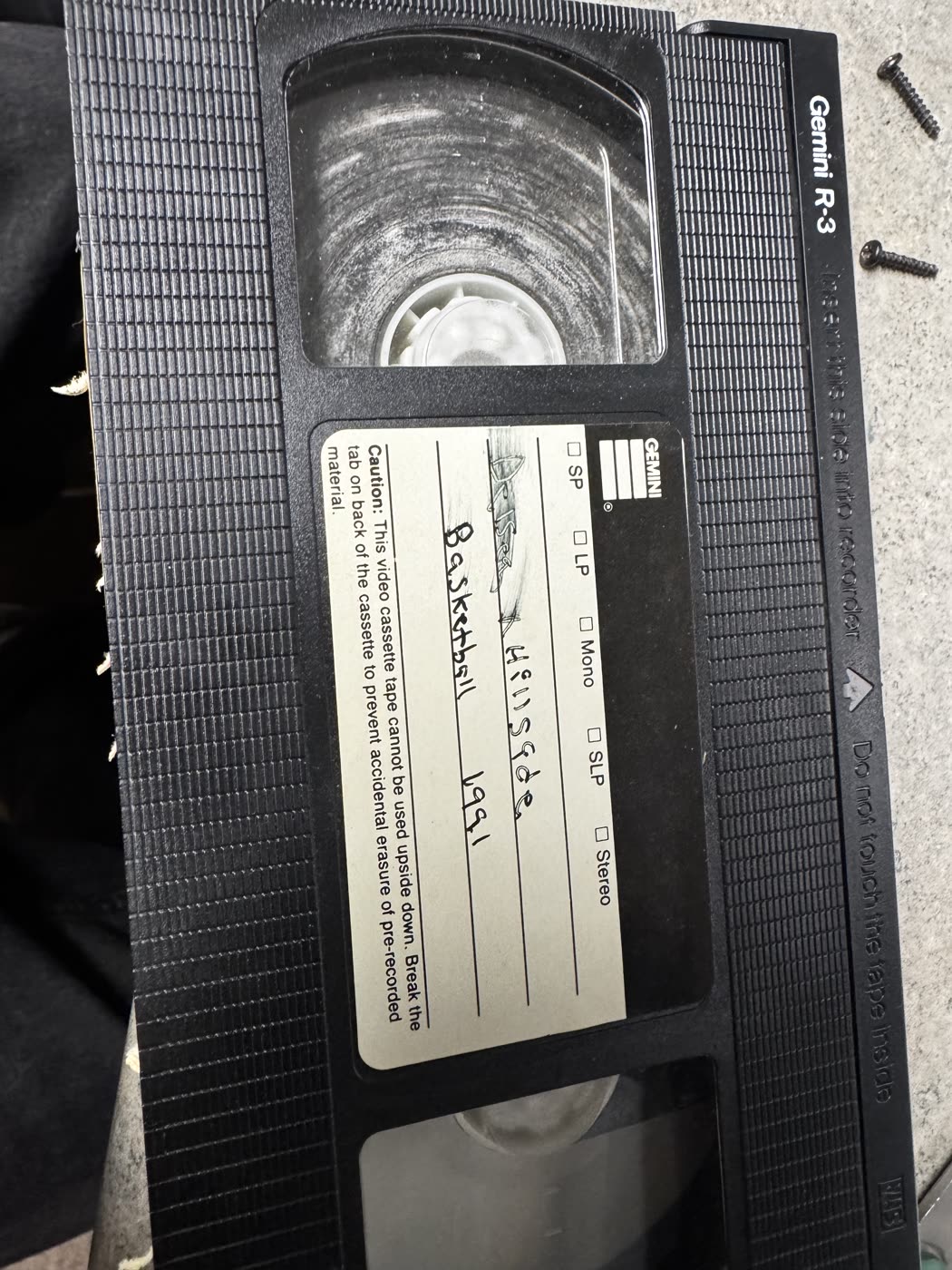 VHS cassette labeled Hillside Basketball 1991 with white mold visible on the tape reel through the window